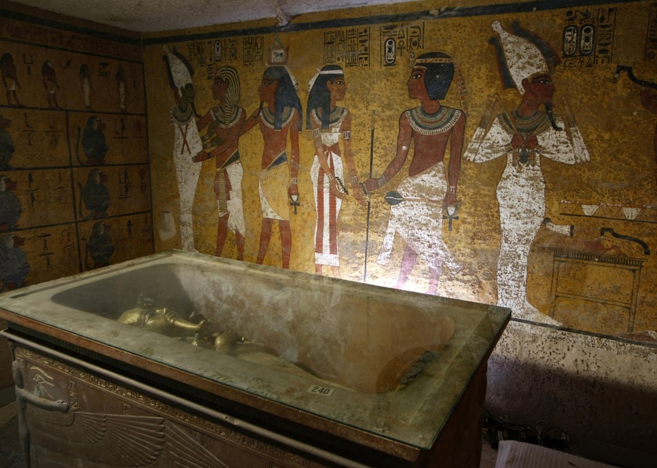default-1630 A golden sarcophagus is shown lying in an elaborate burial chamber. The wall behind it is colourfully painted with figures.