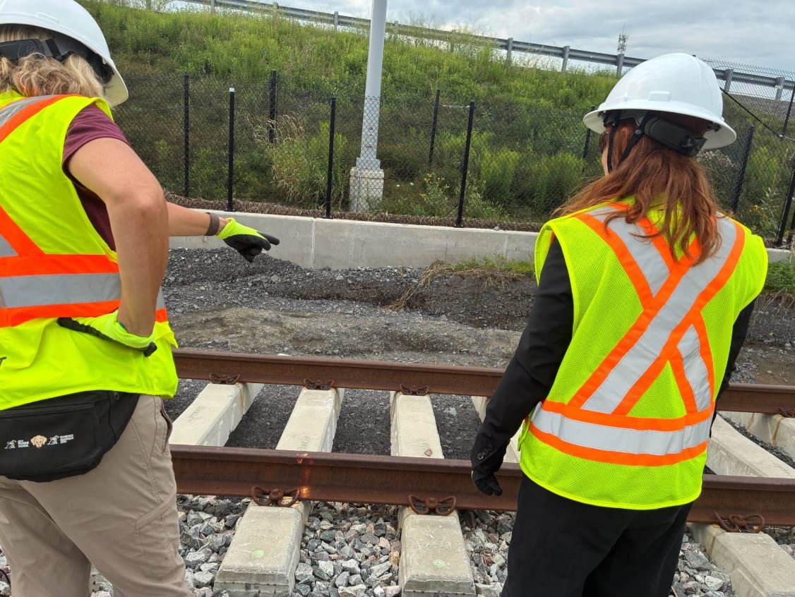 Someone in a construction vest points at a section of light rail track.