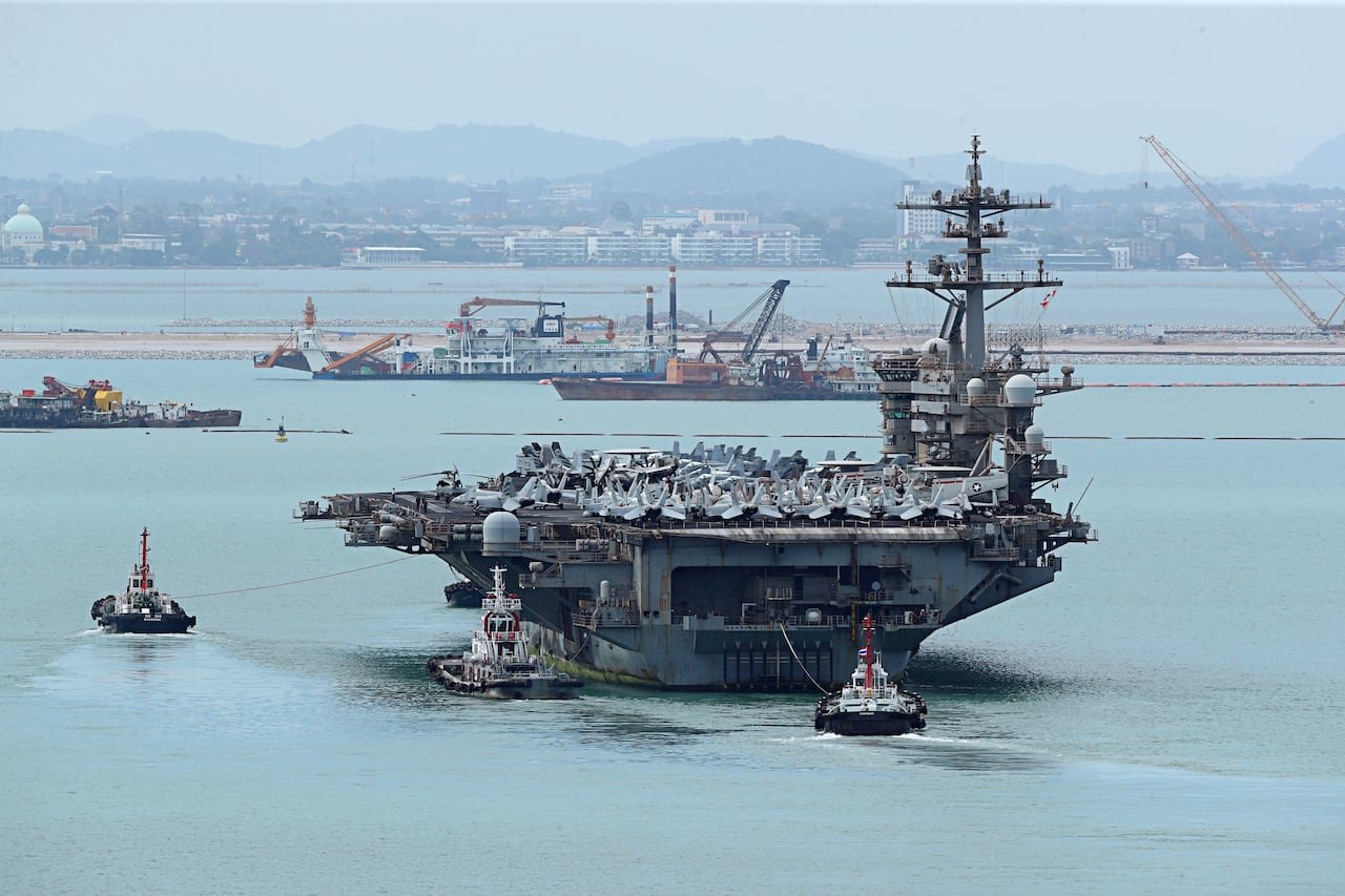 Three tugboats near an aircraft carrier.