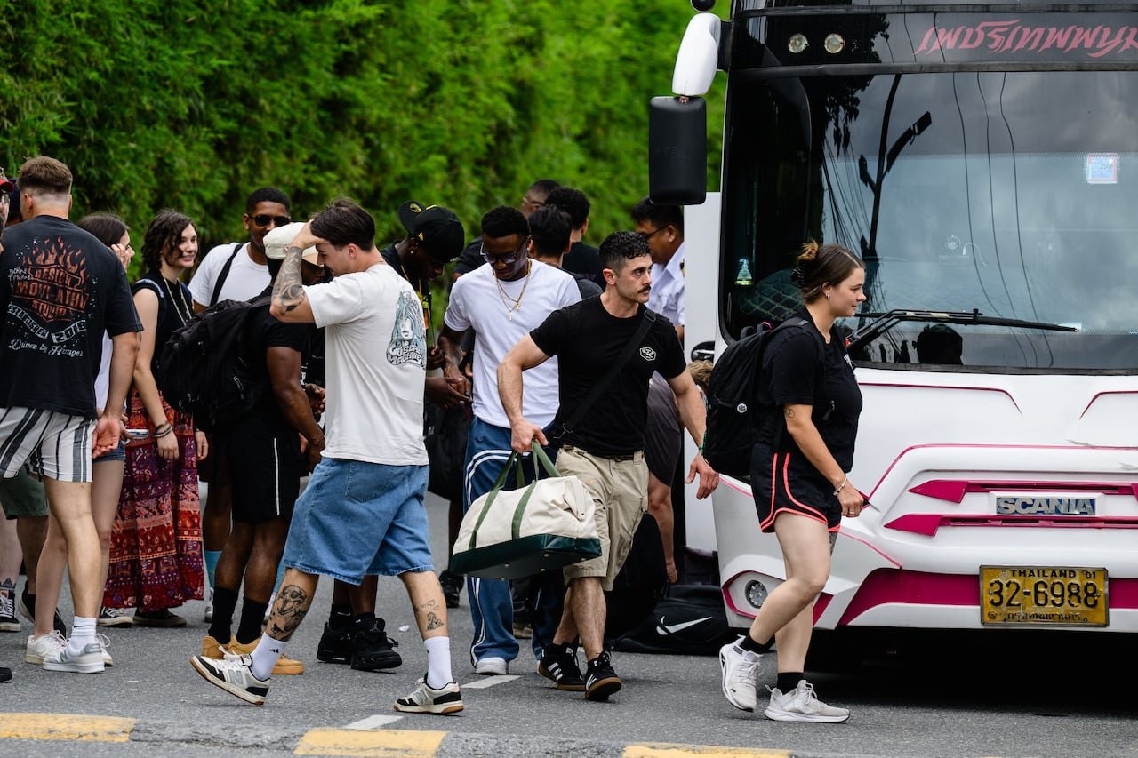 Men and women in civilian clothes outside a bus with a Thailand licence plate.
